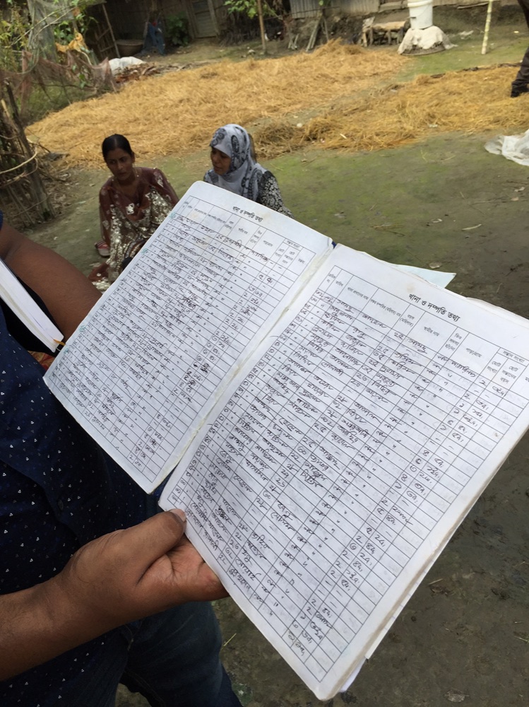 Field team reviewing a handwritten participant ledger in a village setting
